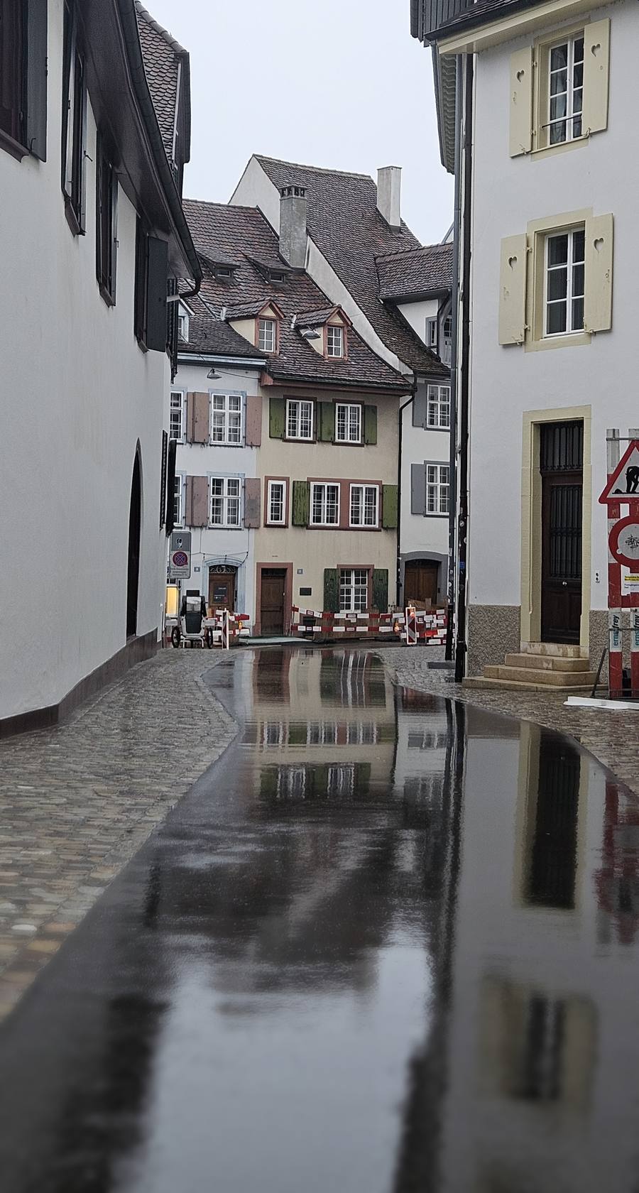Regennasse Gasse in der Basler Altstadt mit historischen Häusern und grünen Fensterläden